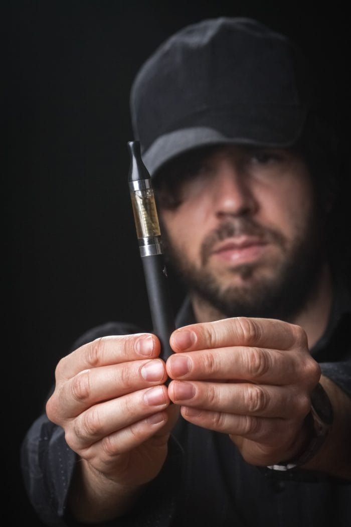 Young man smoking electronic cigarette on black background
