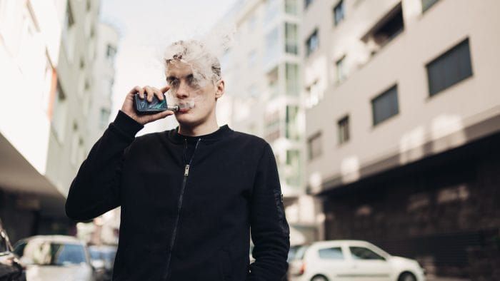 Young man using electronic cigarette to smoke in public places.Smoke restriction, smoking ban.Using vaping device with flavoured liquid.Smoking habit, nicotine addict, tobacco industry