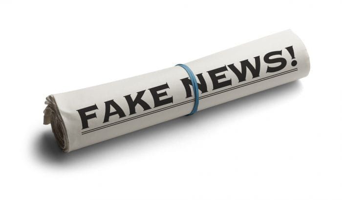 Rolled Up Newspaper with Headline of Fake News Isolated on White Background.