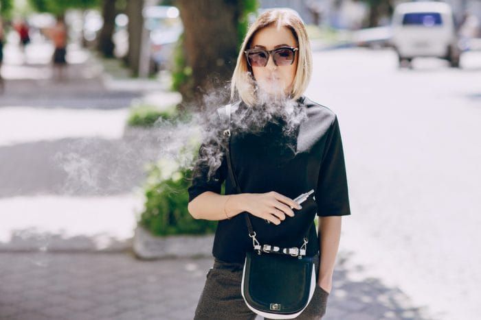 young beautiful girl enjoys electronic cigarette the Sunny weather