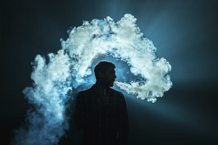 The man smoke an electronic cigarette on the dark background