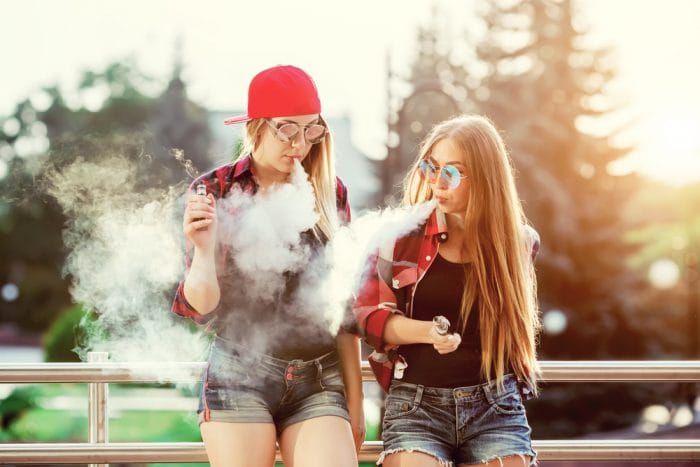 Two women vaping outdoor. The evening sunset over the city. Toned image.