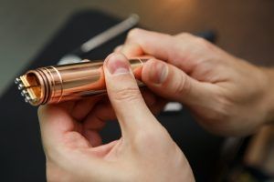 Specialist repairing broken luxury golden mech mod vaping device.Master fixing broken ecig vaporizer gadget.Technician repair gold vape pen.Modern electronic cigarette maintenance.Repair broken vape