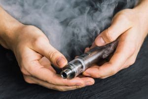 vape device at cloud of vapor background. Vape concept, toned Man hand shows vape device at cloud of vapor background. Vape co