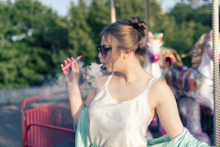 blonde young lady in a spring outfit, smoking a pink colored vape kit