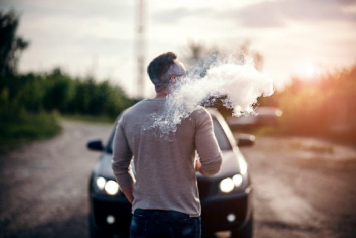 Men with beard vaping outdoor in sunglasses, focus on steam