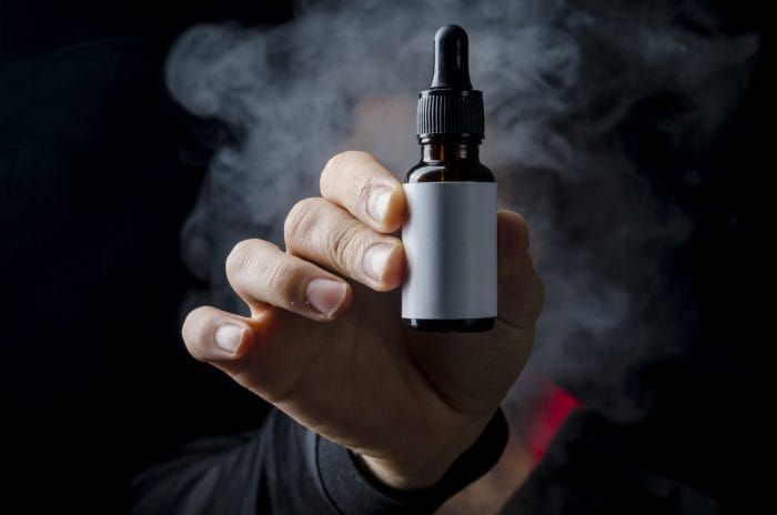 holding e liquid bottle for electronic cigarette, isolated ecig flavor bottle for vape devices over a black background