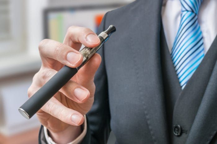 Businessman holds e-xigarette or vaporizer in hand.