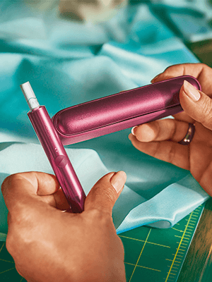 A pair of hands holding a plum-coloured IQOS ILUMA pen and pen holder.