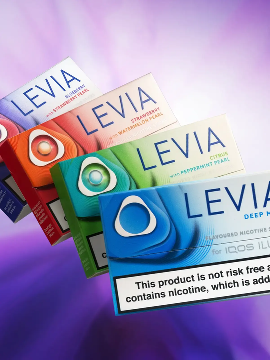 Four packs of different IQOS LEVIA Sticks floating side by side on a stylised purple background