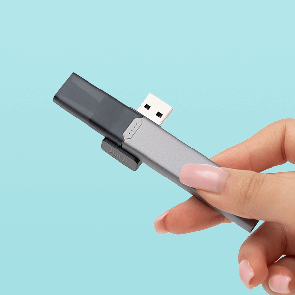 A JUUL2 device shown in hand connected to its magnetic usb charger